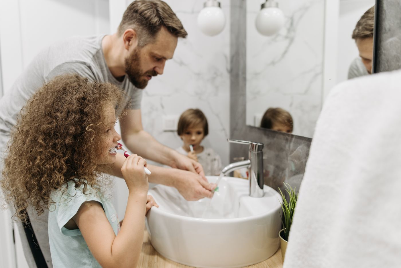 Father and daughter washing hands together at the sink of a bright remodeled bathroom